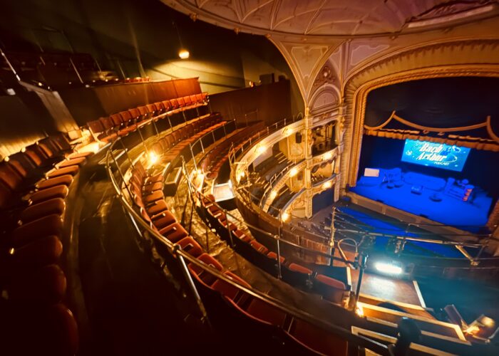 Gallery PIc – Credit Tyne Theatre & Opera House A photograph of of the Tyne Theatre & Opera House auditorium, taken from the Gallery. The photo shows the newly restored Gallery, its new red Heritage seating, and the stage which sits below on the right hand side of the image and is washed in blue lighting.