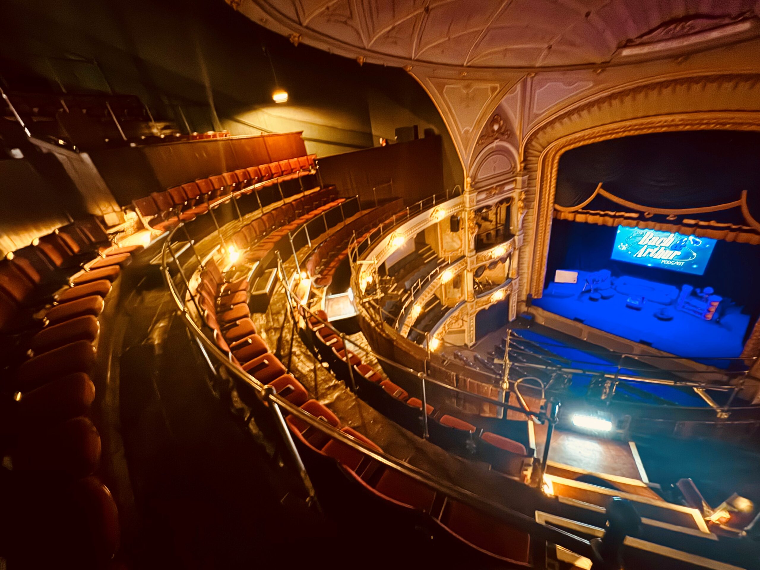 Gallery PIc – Credit Tyne Theatre & Opera House A photograph of of the Tyne Theatre & Opera House auditorium, taken from the Gallery. The photo shows the newly restored Gallery, its new red Heritage seating, and the stage which sits below on the right hand side of the image and is washed in blue lighting.